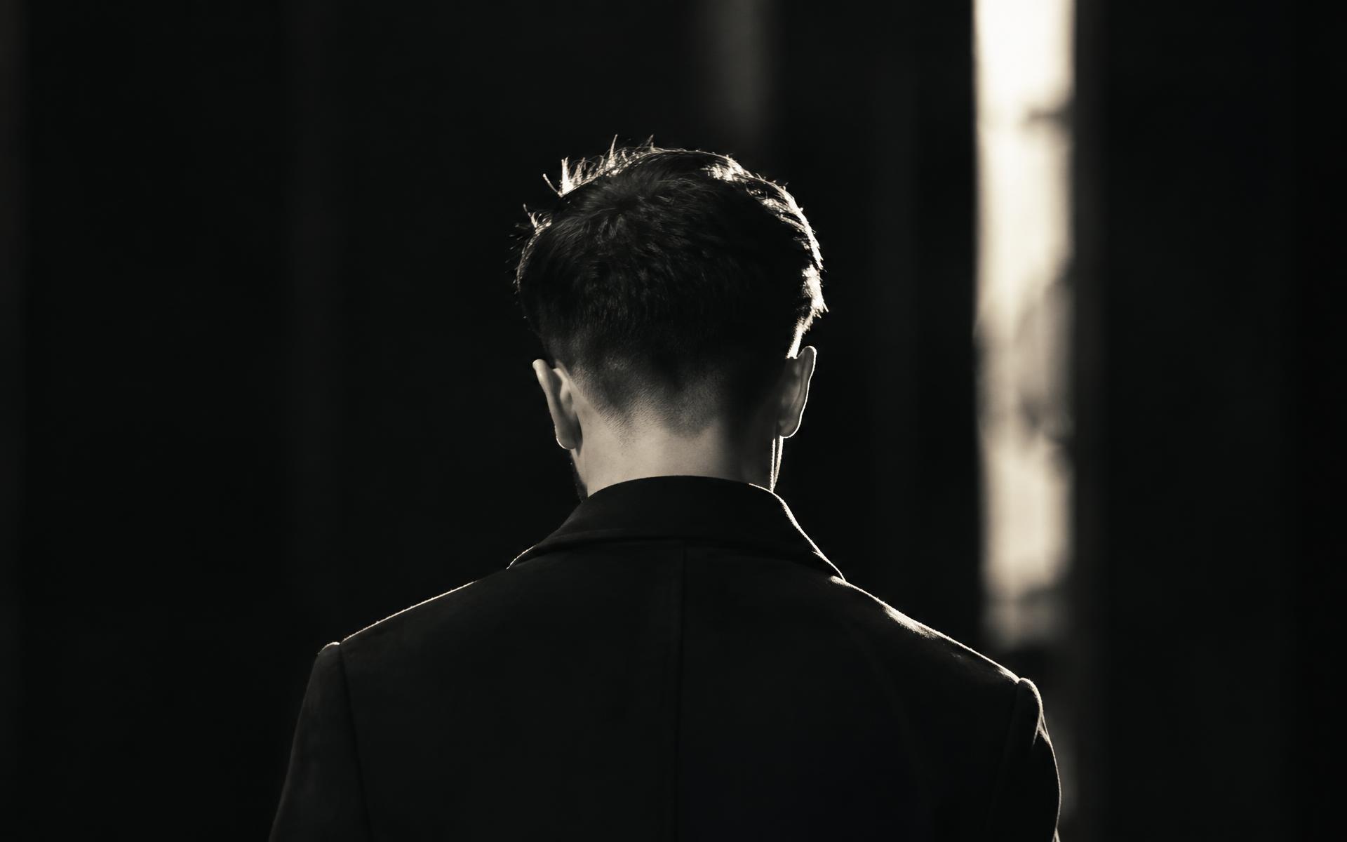 Back view of a man with a precise fade, rim-lit in darkness